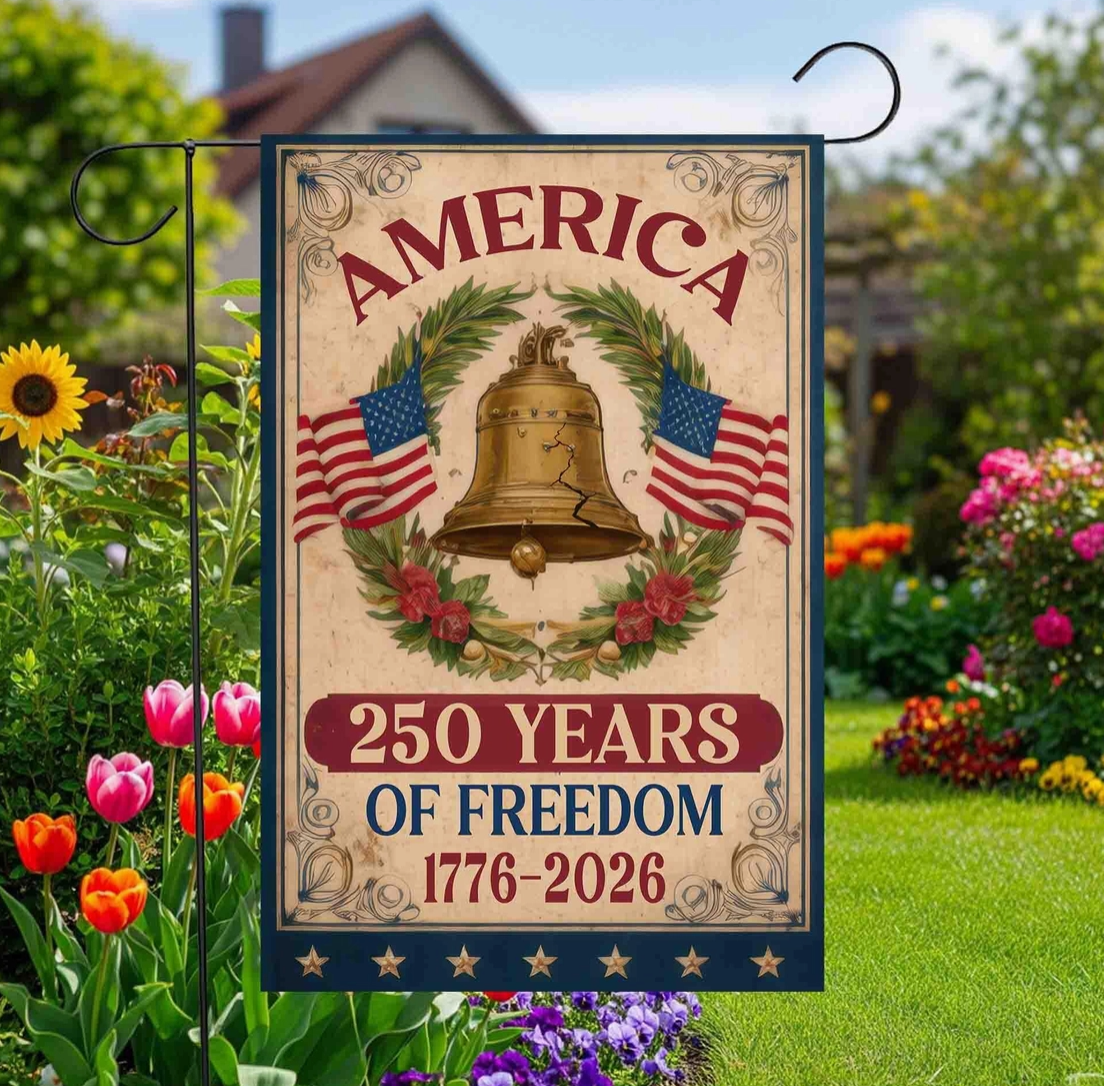 Decorative garden flag celebrating America's 250th anniversary of freedom with a bell and American flags in a garden setting.