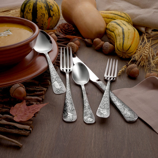 Silver cutlery set on a wooden surface with pumpkins and soup bowl in the background