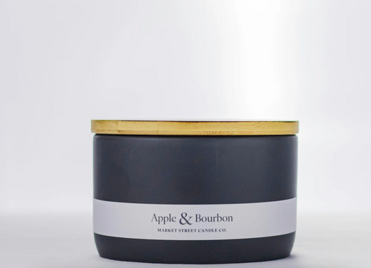 Market Street Candle Co. Apple & Bourbon 16 oz three-wick candle in a charcoal ceramic vessel with gold-tone lid.