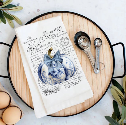 Tea towel with blue pumpkin design on a wooden board with measuring spoons and eggs.