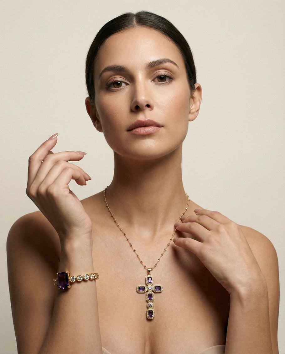 Woman wearing a gold necklace with a cross pendant and amethyst stones on a beige background