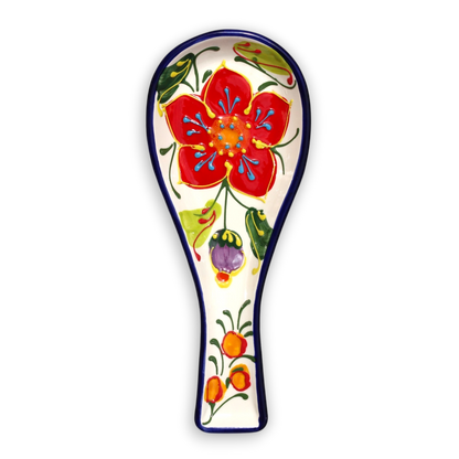 A ceramic spoon rest with a hand-painted floral design featuring a large red flower, green leaves, and orange berries on a white background with a dark blue rim.