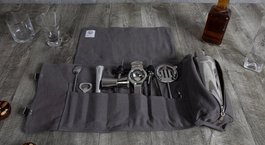 Set of bar tools on a gray mat with bottles and glasses in the background