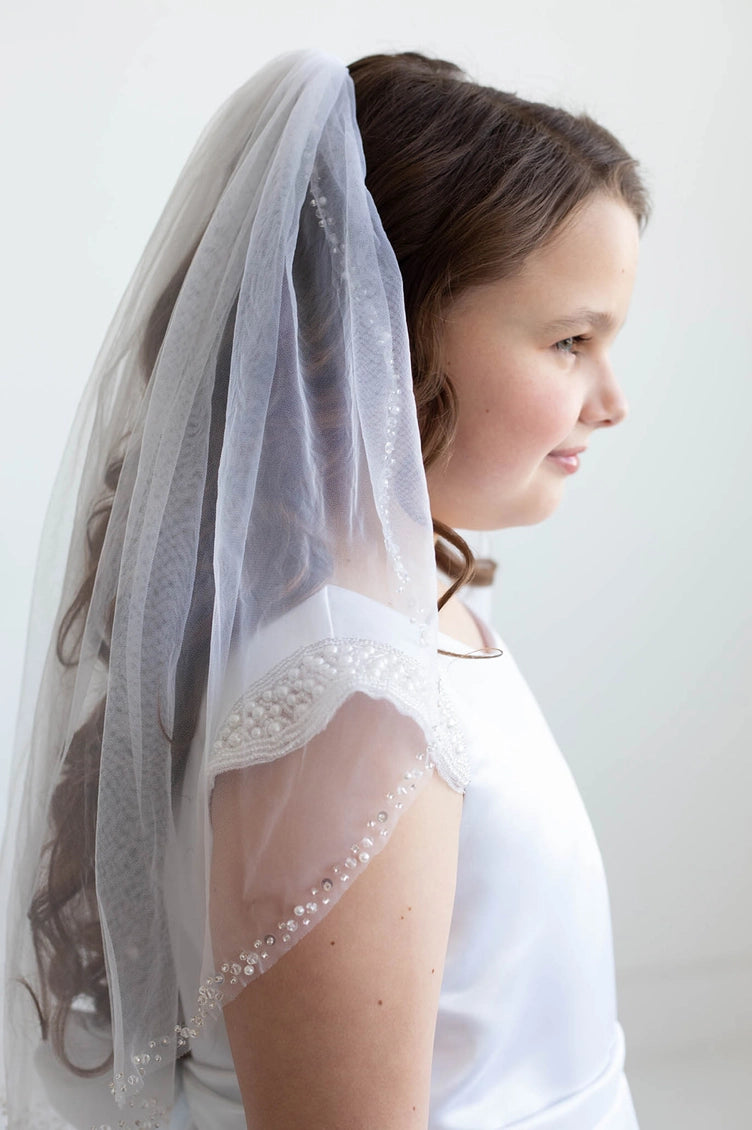 Young girl wearing a communion white veil with lace details on a plain background