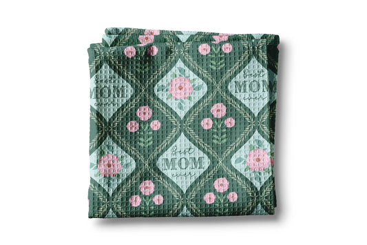 Folded quilt with floral pattern and 'Best Mom' text on a white background