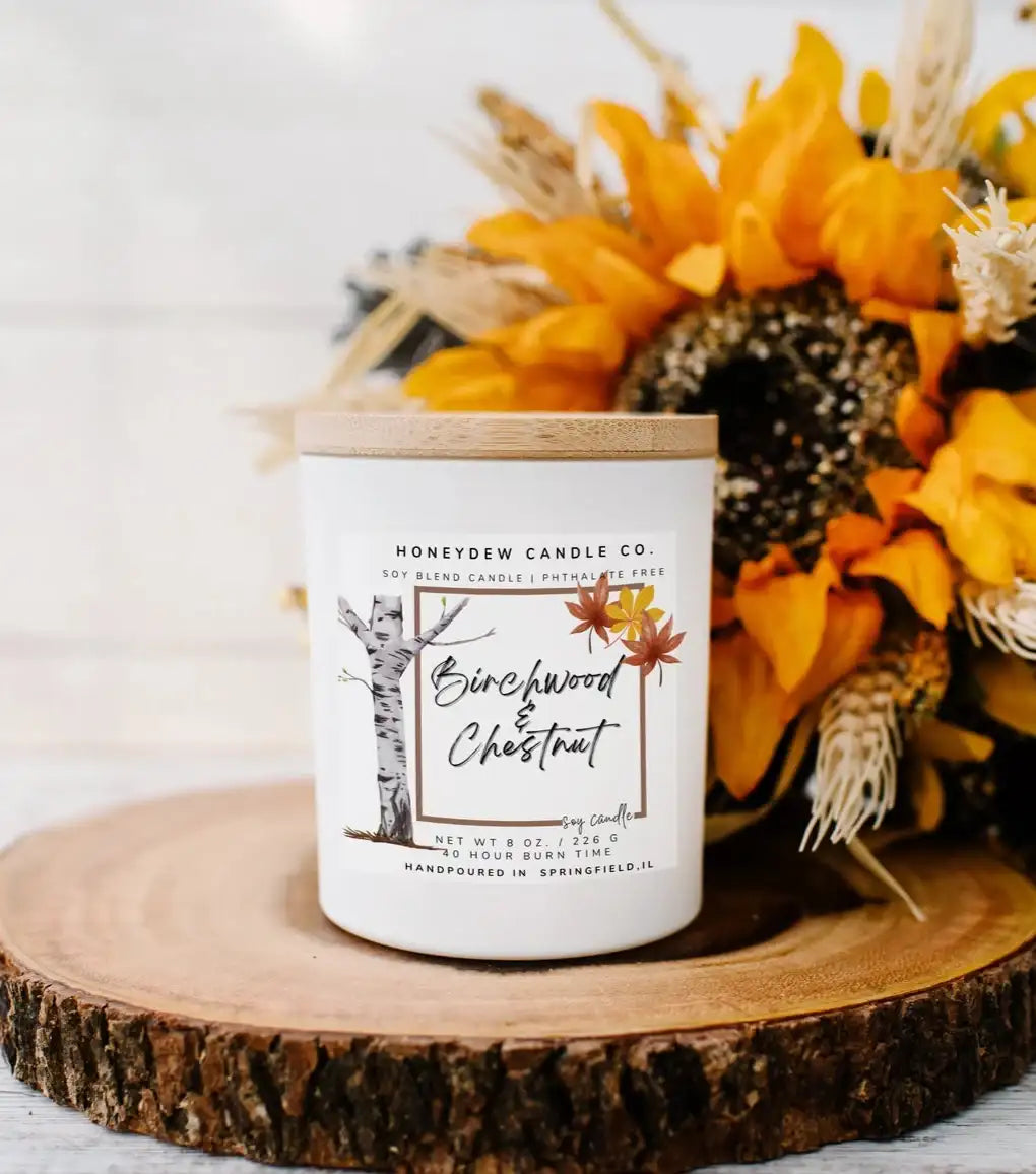 Candle labeled 'Honeysuckle Chestnut' on a wooden coaster with sunflowers and pinecones.