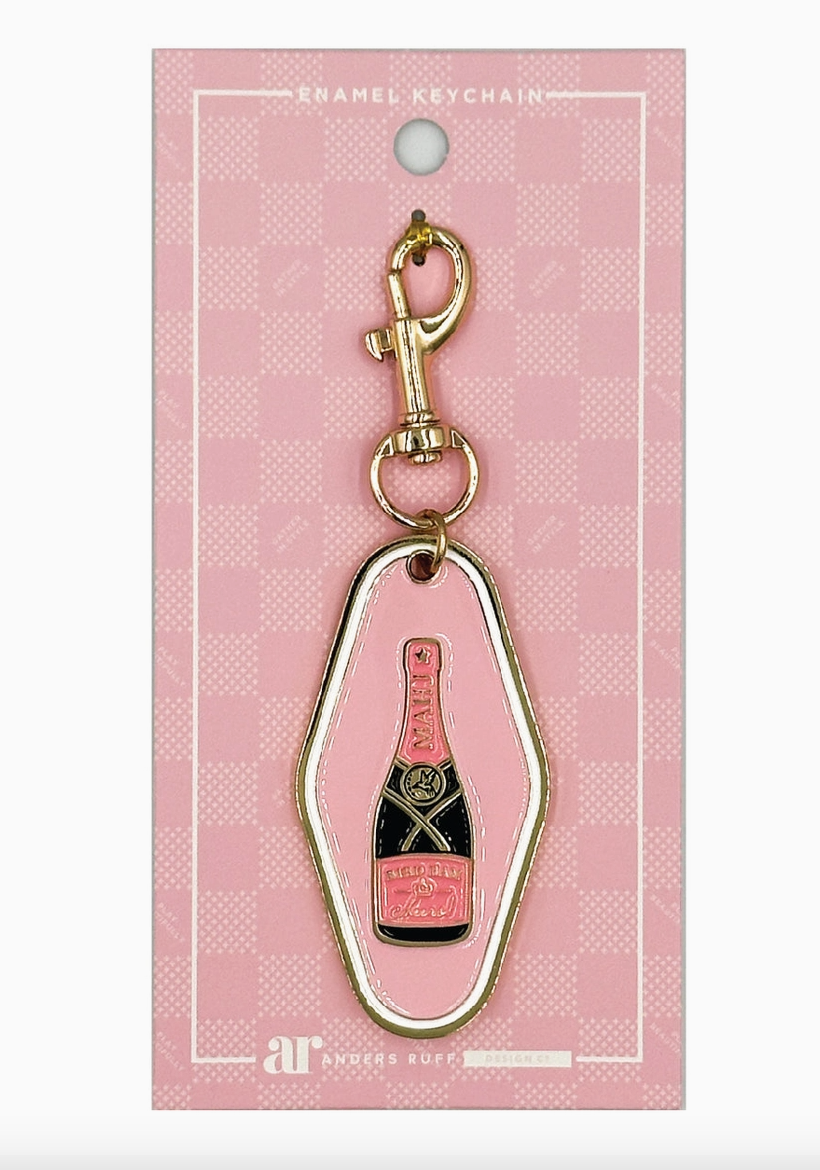 Bird Bam Cheers Mahjong keychain charm by Anders Ruff featuring a blush pink enamel hotel-style tag with champagne bottle design and gold-tone lobster clasp.
