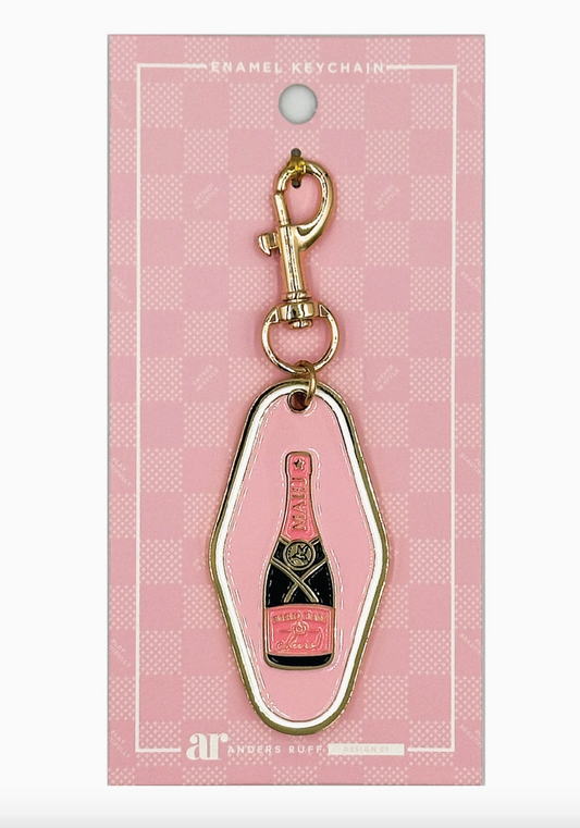 Bird Bam Cheers Mahjong keychain charm by Anders Ruff featuring a blush pink enamel hotel-style tag with champagne bottle design and gold-tone lobster clasp.