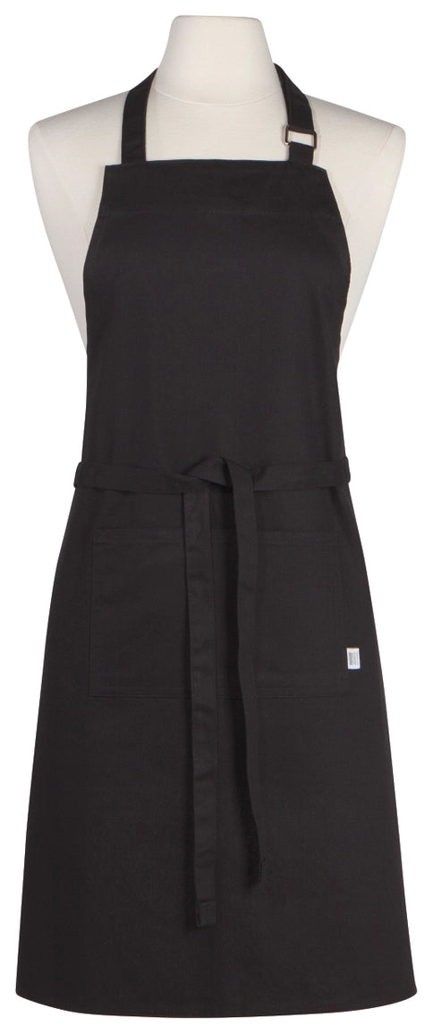 A black bib apron displayed on a white mannequin torso against a plain white background. The apron has a neck strap, waist tie, and a small white tag on the lower right side.