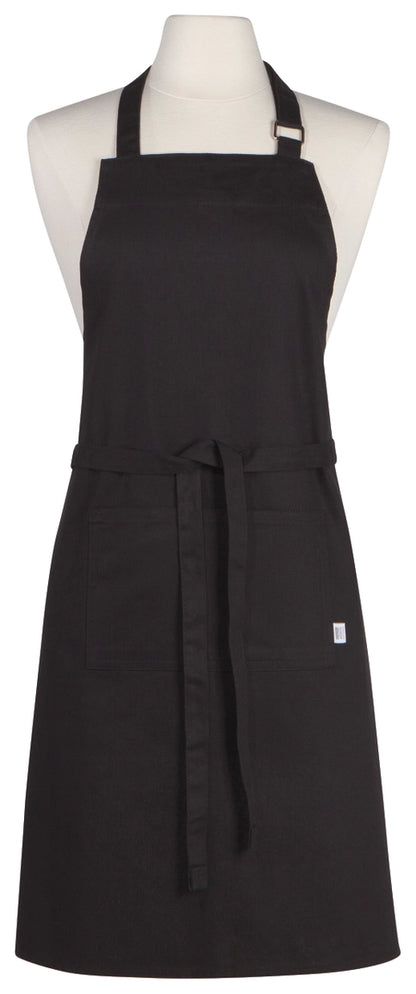 A black bib apron displayed on a white mannequin torso against a plain white background. The apron has a neck strap, waist tie, and a small white tag on the lower right side.