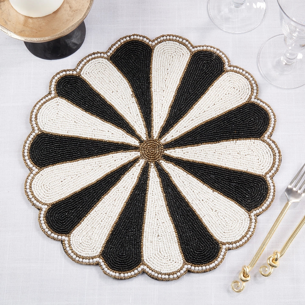 Decorative black and white beaded placemat on a table with cutlery and glasses.