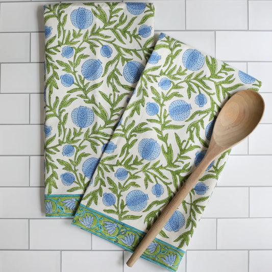 Two patterned towels with blue and green design on a white tiled surface, accompanied by a wooden spoon.