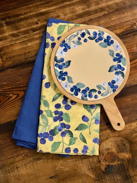 Decorative hand mirror and towels with blueberry pattern on a wooden surface
