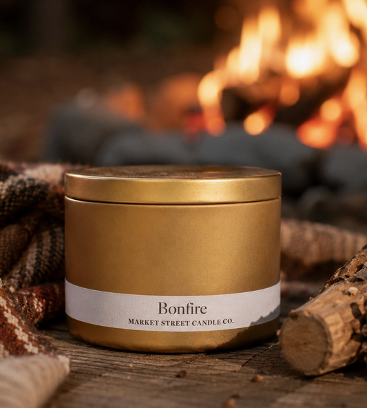 Bonfire Travel Tin candle in a gold metal tin styled beside firewood and a glowing fireplace for a cozy fireside setting.