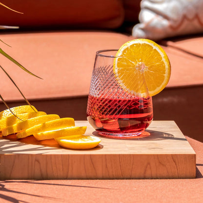 Glass of red cocktail with lemon slices on a wooden board outdoors