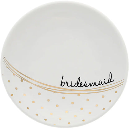 A white round ceramic plate with gold polka dots and gold wavy lines, featuring the word 'bridesmaid' in black script across the lower half.