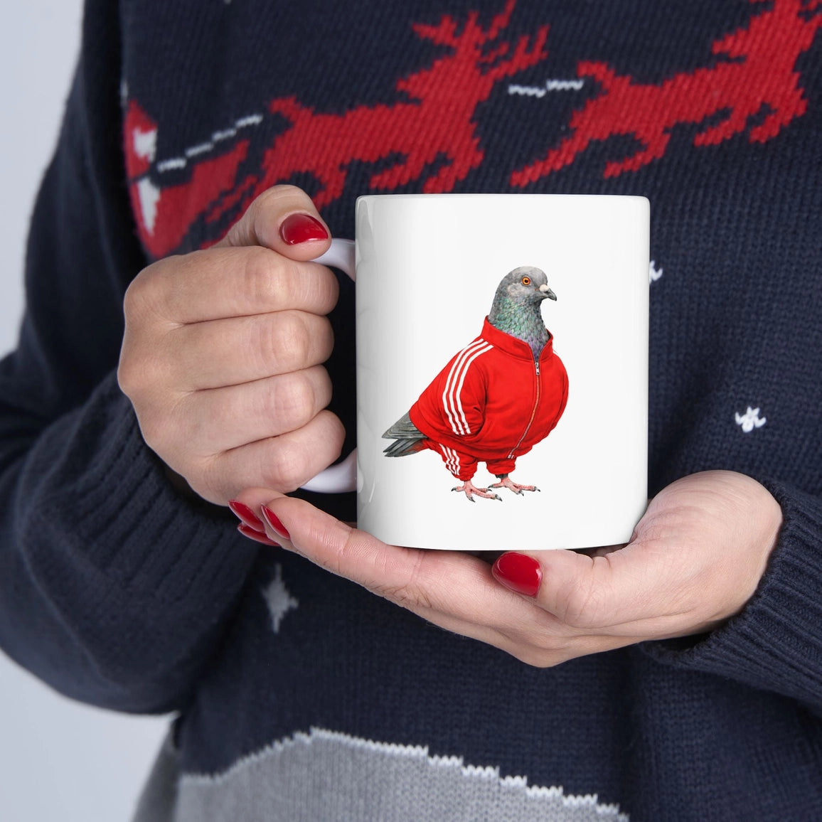 Person holding a mug with a pigeon in a red jacket design, wearing a dark sweater with red deer patterns.