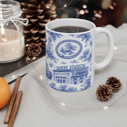 White mug with blue design featuring 'Yankee Stadium' on a table with decorative items.