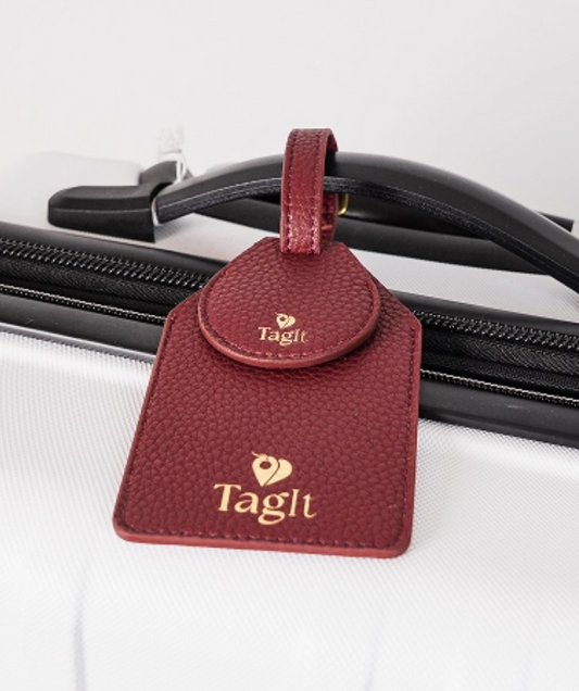 Burgundy AirTag luggage tag attached to cream suitcase showing concealed tracker pocket and vegan leather texture