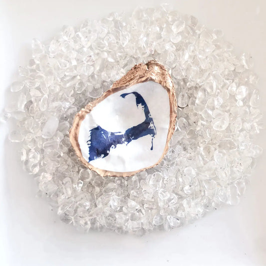 Decorative oyster shell with blue interior  of a map of cape Cod on a bed of clear pebbles