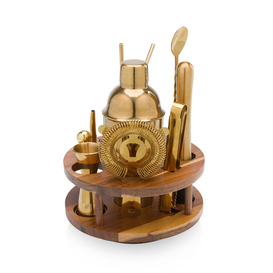 Set of gold cocktail tools on a wooden stand against a white background