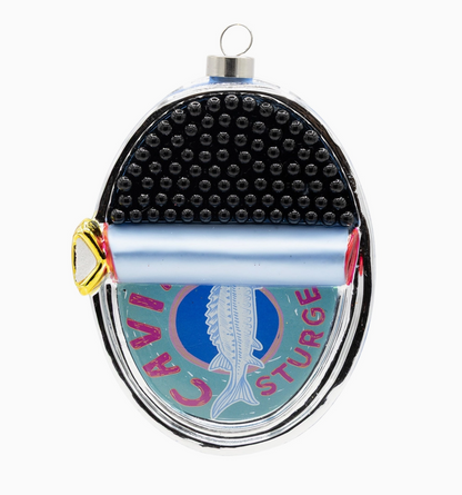 An oval Christmas ornament styled like a Camper-Sturge sex toy, featuring a black textured top, a light blue rolled cylinder, and a lower section with a white fish on a blue background and pink text reading 'CAMPER STURGE'.