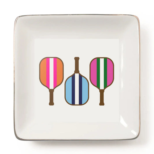 A square white ceramic plate with a metallic gold rim, featuring a graphic print of three paddle-shaped objects with colorful vertical stripes (orange, pink, white; blue, navy, white; pink, green, white) on a clean white background.