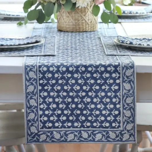 Blue and white patterned table runner on a dining table with plates and a basket.