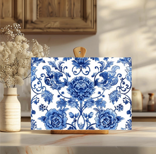 Floral patterned cutting board on a wooden surface with a vase of flowers in the background.