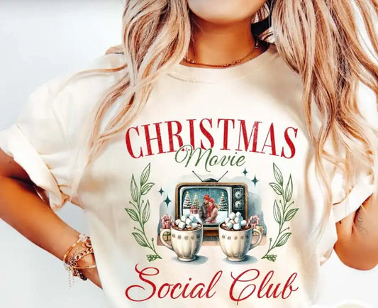 Person wearing a white t-shirt with 'Christmas Movie Social Club' design.