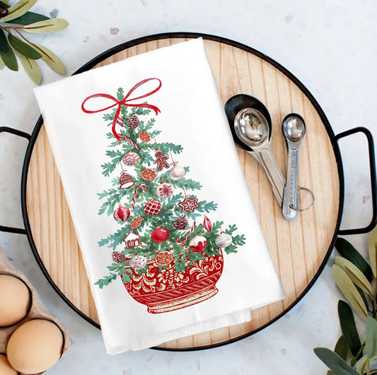 Decorative towel with Christmas tree design on a wooden cutting board with measuring spoons.