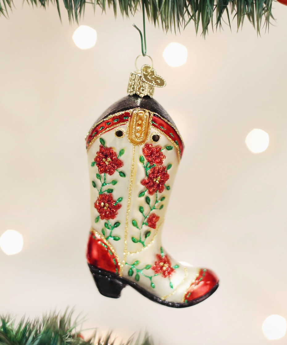 Cowgirl boot glass Christmas ornament with red flowers green vines and gold details hanging on a Christmas tree
