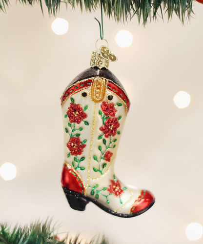 Cowgirl boot glass Christmas ornament with red flowers green vines and gold details hanging on a Christmas tree