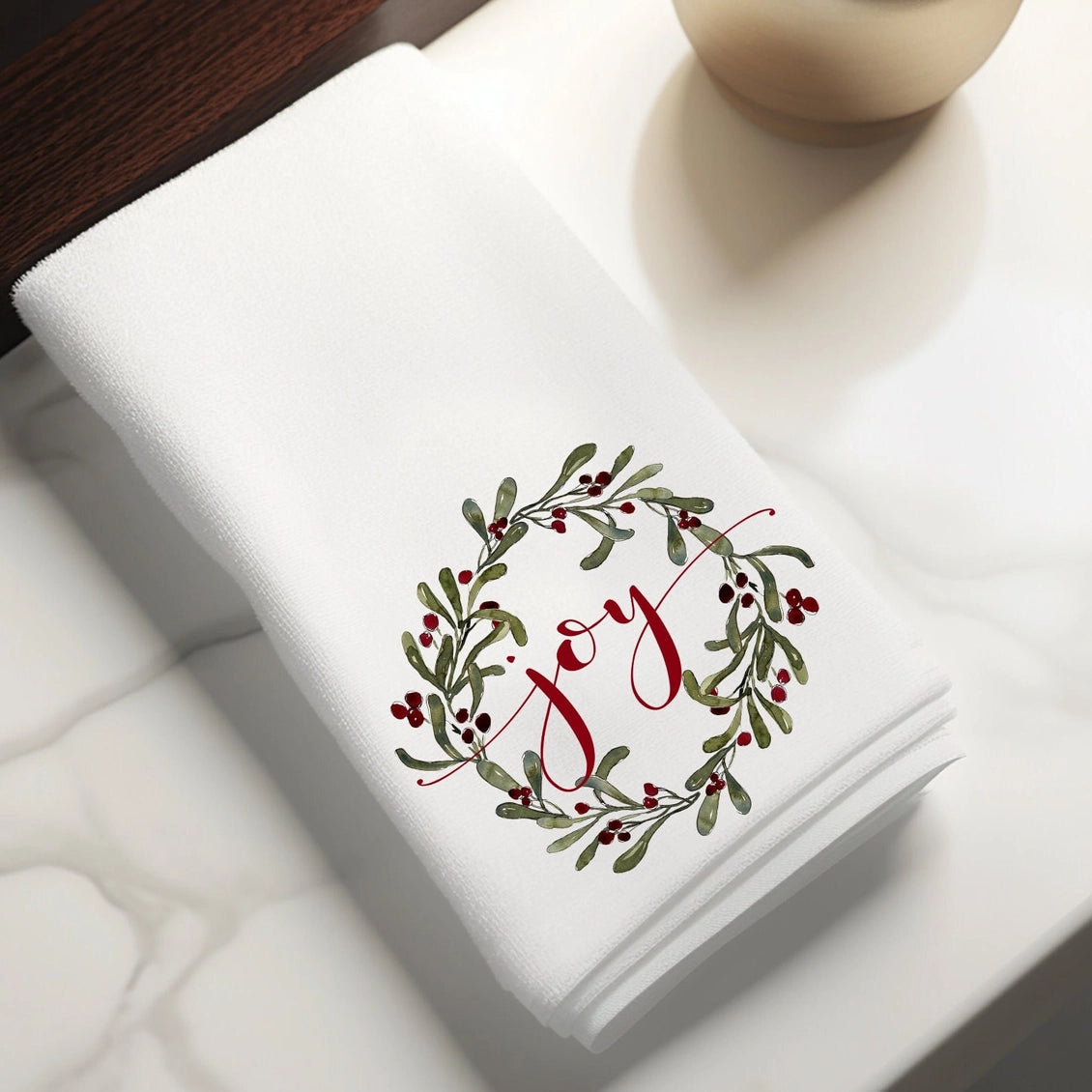 Folded white towel with 'Joy' design on a white surface