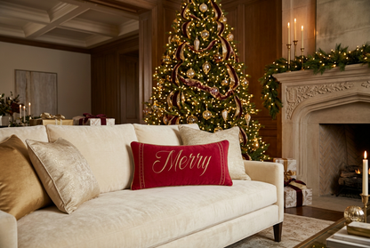 Red rectangular Christmas lumbar throw pillow featuring large embroidered metallic-gold Merry script, decorative gold vertical side borders, and coordinating gold piping.