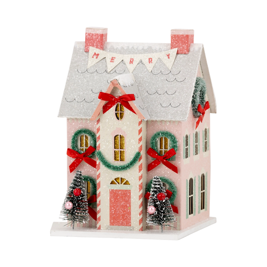 Decorative Christmas house with candy cane design, wreaths, and small trees on a white background.