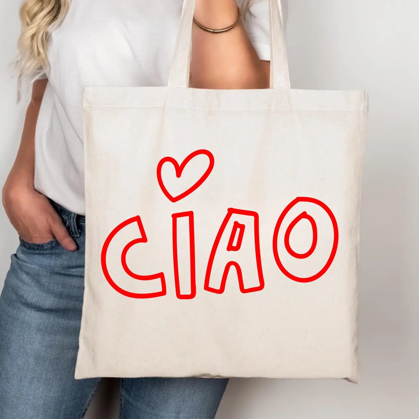 A person wearing a white t-shirt and blue jeans holds a cream-colored canvas tote bag with the word 'CIAO' and a heart drawn in red outline.