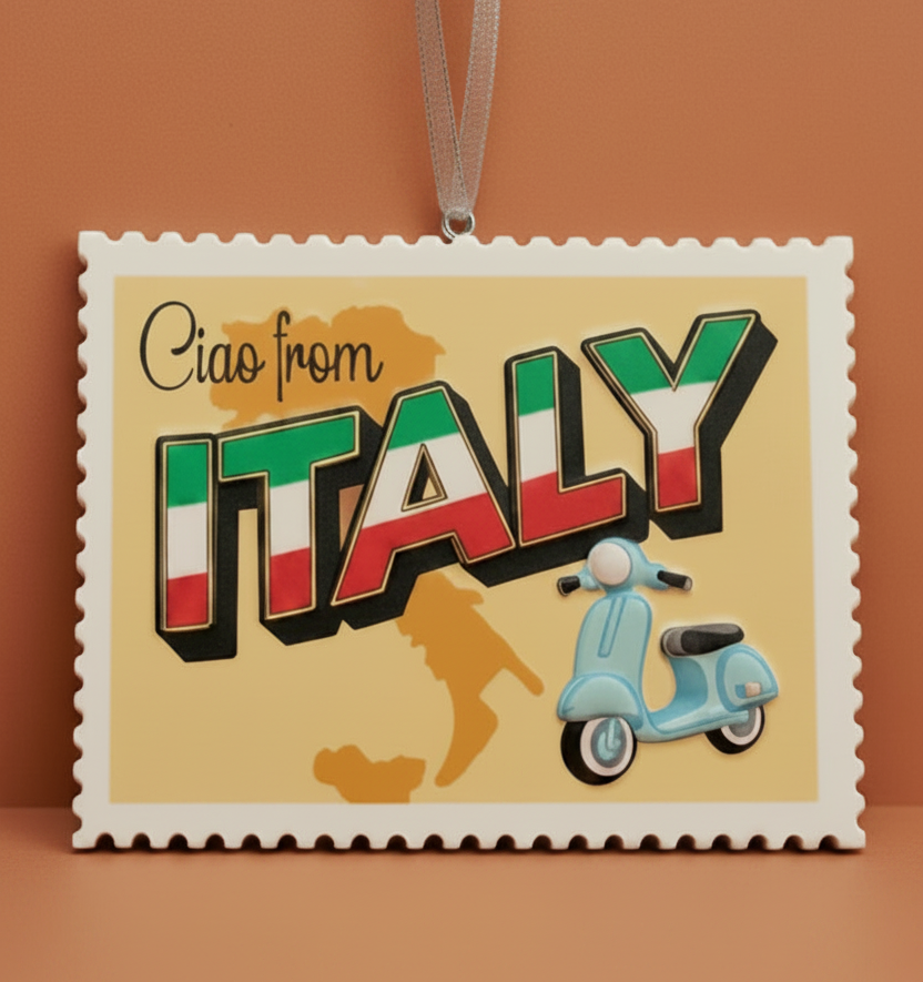 A square decorative Italy-themed ornament or plaque with scalloped edges, hanging from a white ribbon. The design reads 'Ciao from ITALY' in large 3D letters filled with the Italian flag colors, with a light blue scooter and yellow map silhouette on a pale yellow background, shown on a dark brown surface.
