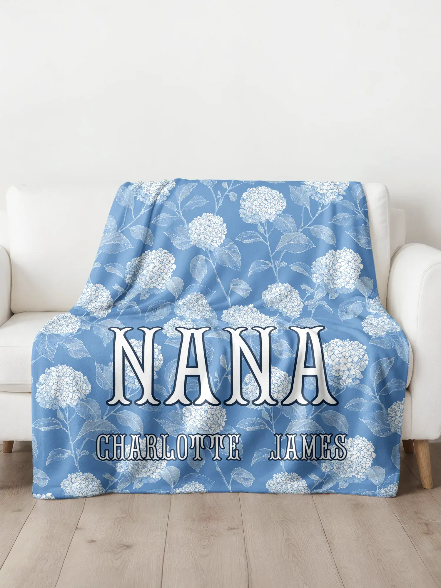 Blue floral blanket with 'Nana' and 'Charlotte James' text on a white couch.