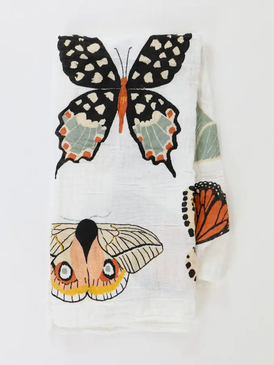 A white textured fabric napkin or tea towel featuring printed illustrations of various butterflies and moths in black, orange, beige, and green.