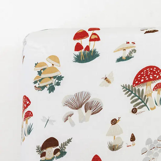 A close-up of a white fabric product, likely a fitted sheet or pillowcase, featuring a whimsical forest mushroom print with red, brown, beige, and green illustrations.