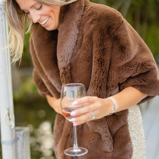 Woman in a brown fur coat holding a glass of red wine outdoors.