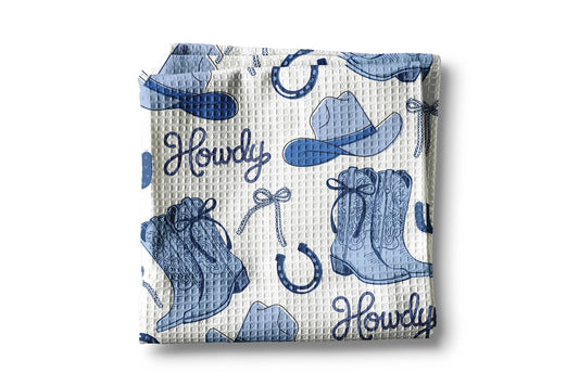 Folded fabric with cowboy-themed pattern including boots, hats, and 'Howdy' text on a white background
