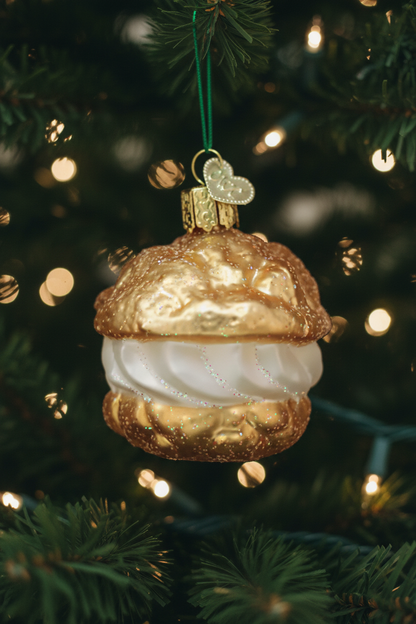 Decorative Christmas ornament resembling a cream puff dessert with gold and white colors, hanging on a tree.