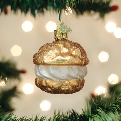 Decorative Christmas ornament shaped like a Cream Puff  hanging on a tree with lights in the background.