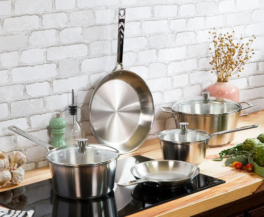 Set of stainless steel cookware on a kitchen counter with a white brick wall background.