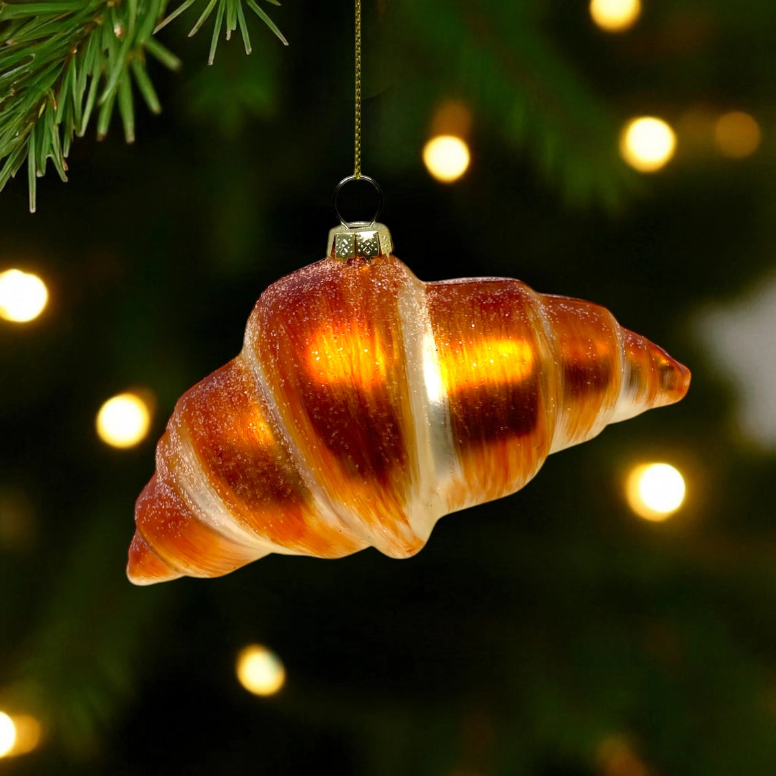 Decorative glass shell ornament hanging on a Christmas tree with blurred lights in the background.