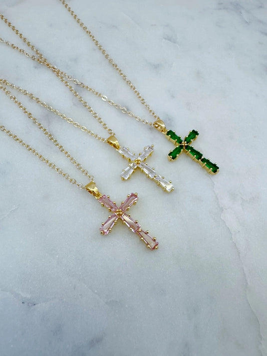 Three cross-shaped necklaces with different colored pendants on a marble surface.