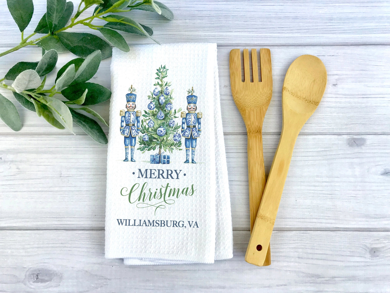Christmas-themed kitchen towel with nutcrackers and tree, next to wooden utensils on a wooden surface.