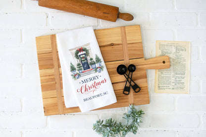 Wooden cutting board with Christmas-themed towel, rolling pin, and greenery on a white brick wall background